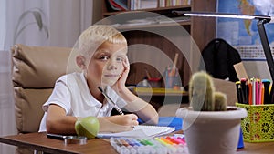 Portrait of a smiling schoolboy boy at his desk at home, he does his homework.