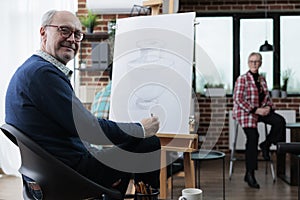 Portrait of smiling senior artist standing in front on white canvas