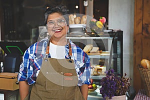 Portrait of a smiling senior Asian barista, hands on pockets, welcoming the customer in a cozy coffee shop. Small business owner