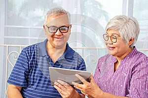 Portrait of smiling senior couple with eyeglasses using electronic tablet while relaxing at the bed room