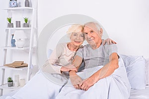 portrait of smiling senior couple resting in bed and looking at camera