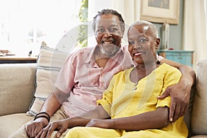 Portrait Of Smiling Senior Couple Sitting On Sofa At Home