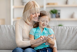 Happy mature woman and granddaughter using cellphone