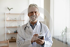 Portrait of smiling senior male doctor use smartphone