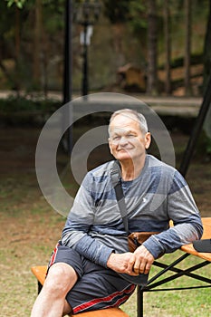 Portrait of smiling senior man sitting and resting on the park bench. Happy old man walking and spends time at the park.