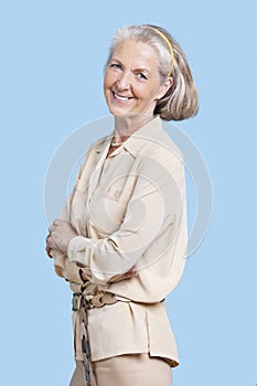 Portrait of smiling senior woman in casuals with arms crossed against blue background