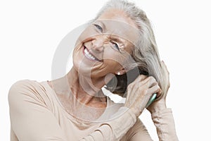 Portrait of smiling senior woman combing her hair against white background