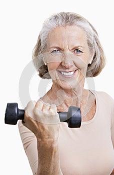 Portrait of smiling senior woman with dumbbell against white background