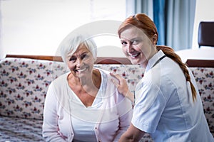 Portrait of smiling senior woman and female doctor in living room