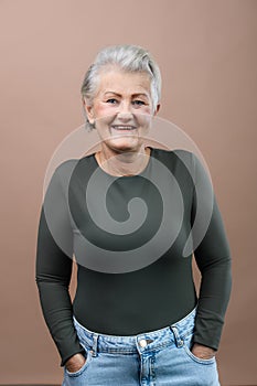 Portrait of smiling senior woman with hands in pockets in studio.