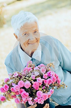 Portrait of smiling senior woman garndmother holding a purple flower pot outdoors