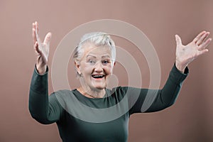 Portrait of smiling senior woman with raised arms in studio.