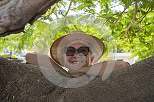 Portrait of smiling senior woman in the shade of a plant in the park with arms resting on branches - active retired seniors and