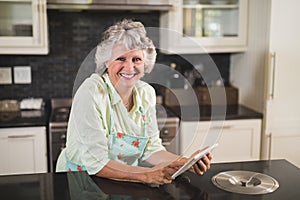 Portrait of smiling senior woman using digital tablet on counter in kitchen