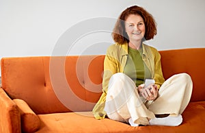 Portrait Of Smiling Senior Woman Using Smartphone While Relaxing On Couch At Home