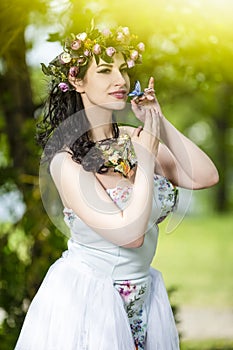 Portrait Smiling Sensual Brunette Female in White Dress Outdoors. Posing with Flowery Chaplet and Butterfly Against Sunlight