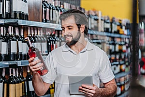 portrait of smiling shop assistant with tablet looking at bottle of wine photo