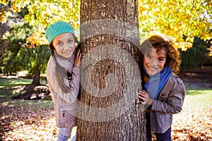 Portrait of smiling siblings leaning on tree trunk at park