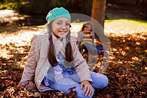 Portrait of smiling siblings sitting at park during autumn