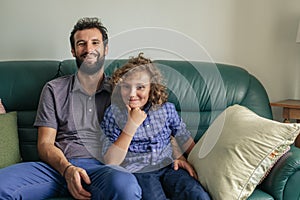Smiling father and young son sitting together on their sofa