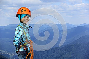 Portrait of a smiling six year old boy wearing helmet and climbing safety harness in mountains