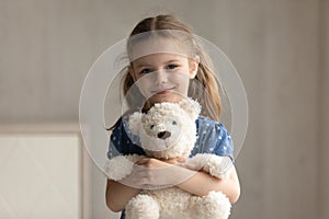 Portrait of smiling small kid girl cuddling favorite fluffy toy.