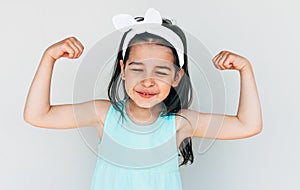 Portrait of a smiling strong little girl showing hands bicep strength make fists feels healthy and happy posing isolated on white