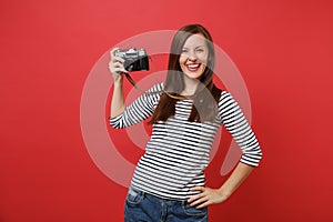 Portrait of smiling stunning young woman in striped clothes holding retro vintage photo camera isolated on bright red