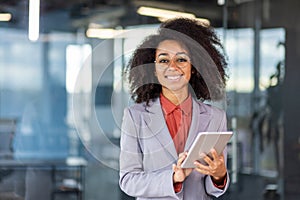 Portrait of a smiling and successful young African American woman in a suit standing in a modern office, holding a