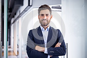 Portrait of a smiling and successful young businessman standing in the office, crossing his arms on his chest and