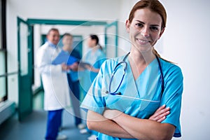 Portrait of smiling surgeon standing with arms crossed in corridor