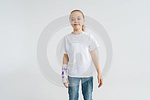 Portrait of smiling sweet little girl with broken hand wrapped in white plaster bandage with colorful draw standing on