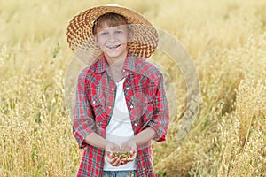 Portrait of smiling teenage farm boy is with oat seeds in cupped palms at ripe field