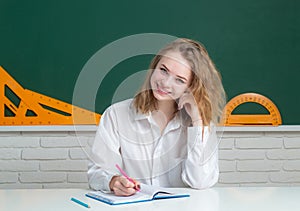 Portrait of smiling teenager girl over blackboard, friendly laughing. Cute college female student in hight school.