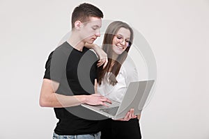 Portrait of a smiling teens boy and girl holding laptop computer while standing and looking in it isolated over white