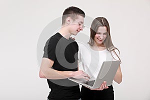 Portrait of a smiling teens boy and girl holding laptop computer while standing and looking in it isolated over white