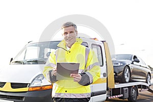 Portrait of smiling tow truck driver with clipboard against sky