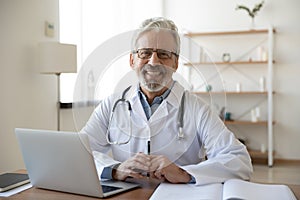 Portrait of smiling trusted middle aged old doctor at workplace. photo