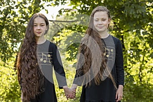 Portrait Smiling Two Sisters With Extra Long Hair Holds Hands In Sunny Day, Girls Wear