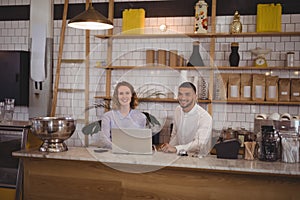 Portrait of smiling waitress and male owner using laptop at counter