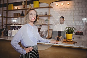 Portrait of smiling waitress standing with hand on hip by counter