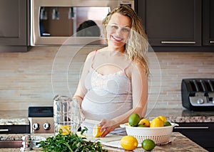 Portrait of smiling white Caucasian blonde pregnant woman cutting citrus lime lemon making juice standing in kitchen