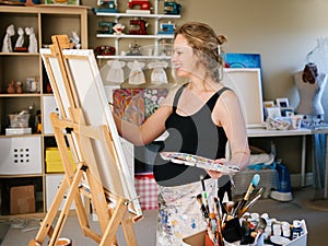 Portrait of smiling white Caucasian young pregnant woman drawing painting standing at easel in home studio