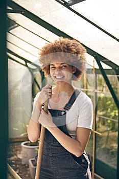 Portrait Of Smiling Woman With Broom Working In Greenhouse At Home