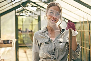 Portrait Of Smiling Woman With Broom Working In Greenhouse At Home