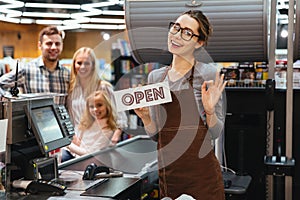 Portrait of smiling woman cashier holding open sign photo