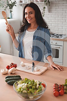 Portrait of smiling woman holding spatula and looking at the camera in the kitchen