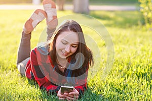 Portrait of a smiling woman lying on green grass and using smartphone outdoors