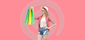 Portrait of smiling woman model looking at colorful shopping bags wearing summer straw hat, checkered shirt, shorts isolated on
