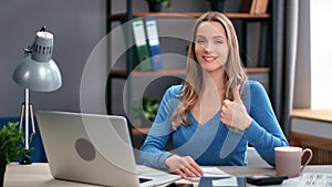 Portrait smiling woman modern worker posing at home office workplace showing cool thumb up gesture